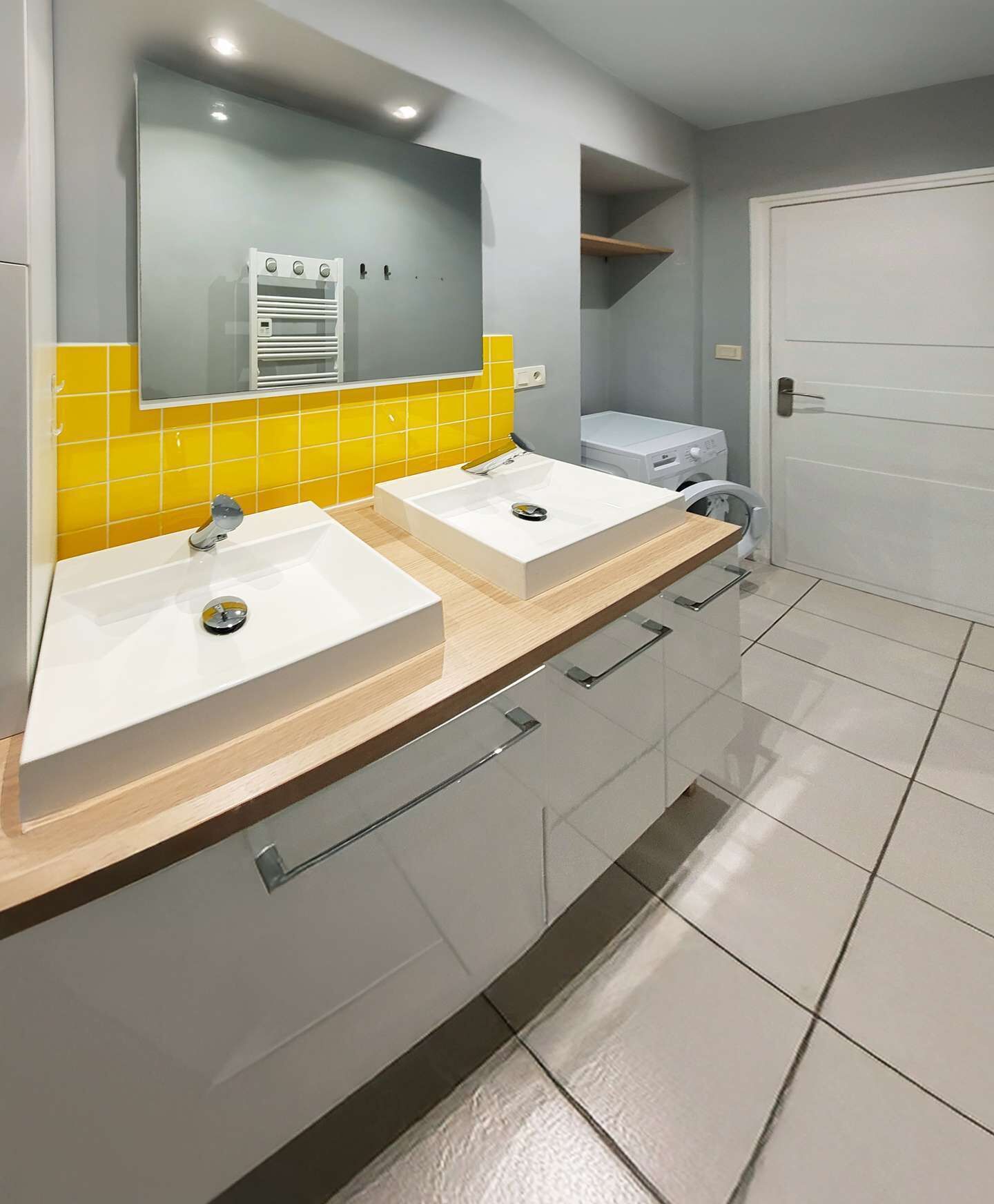 Een badkamer met twee wasbakken, een spiegel, een wasmachine en een deur.