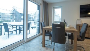 Un espace repas moderne avec une grande fenêtre, une table en bois et des chaises noires.