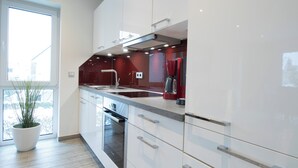 Une cuisine moderne avec des meubles blancs, un évier en acier inoxydable et un appareil électroménager rouge.