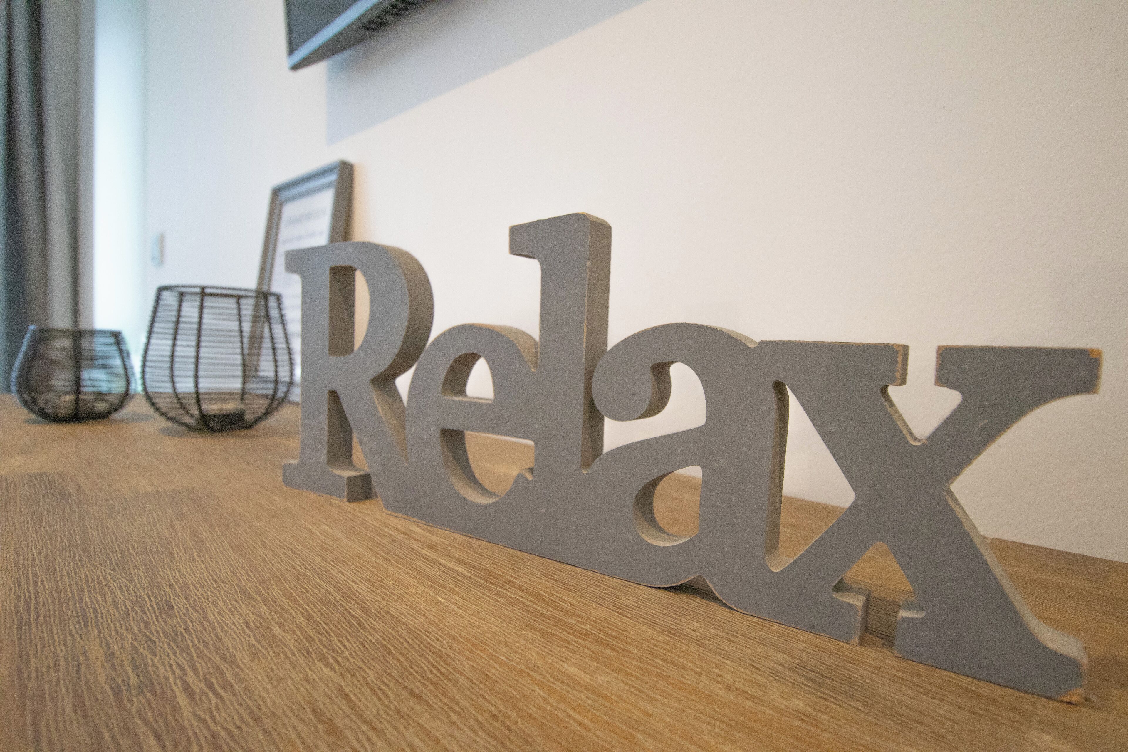 A wooden table with a gray metal sign spelling "Relax" on it.