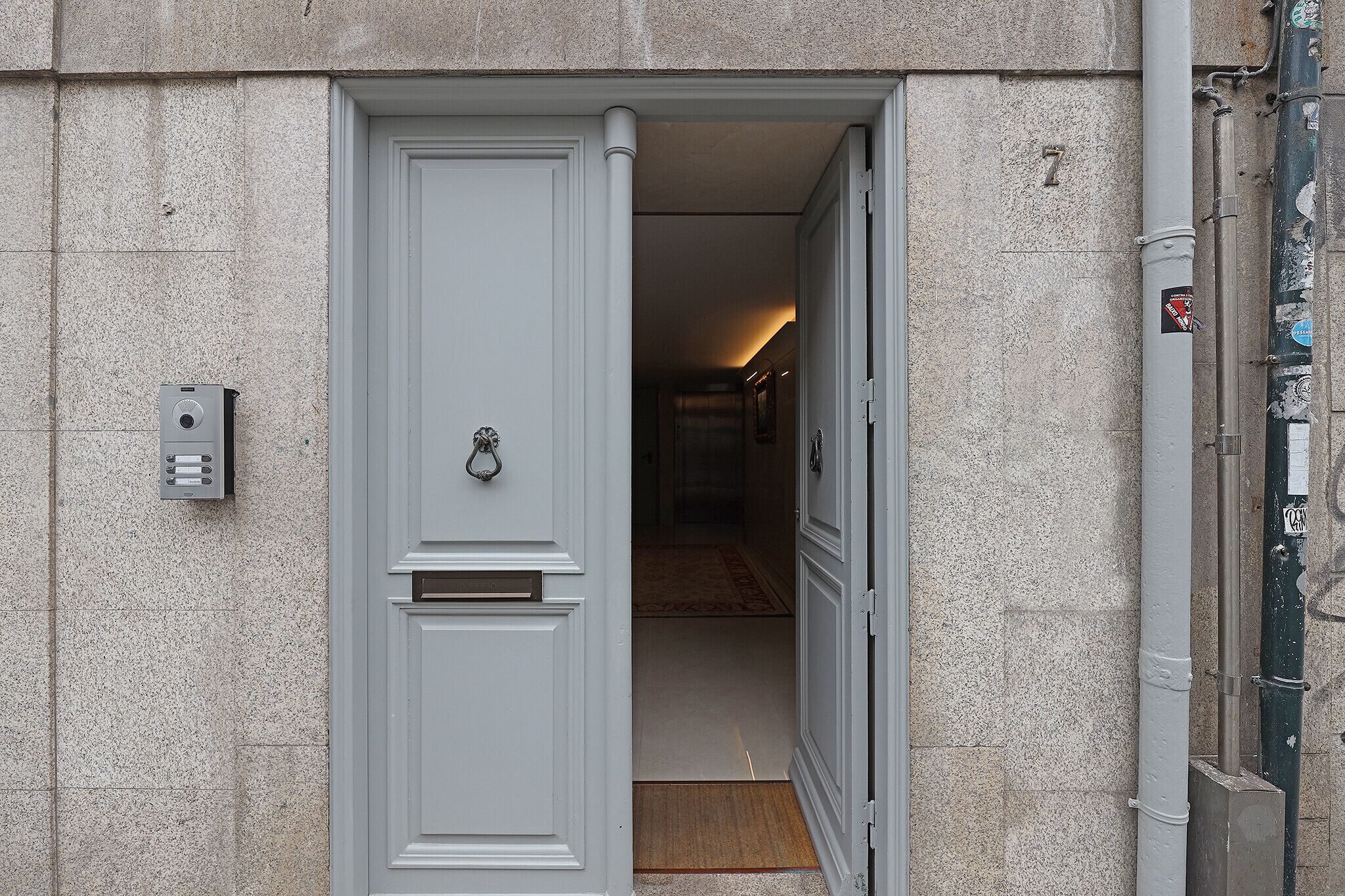 A hotel entrance with a white door, a mail slot, and a small mailbox on the wall.