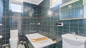 A bathroom with dark blue tiles, a white toilet, a bathtub, and a sink. - Golden-Sands- 3-66-Ocean-Pde (The Entrance)