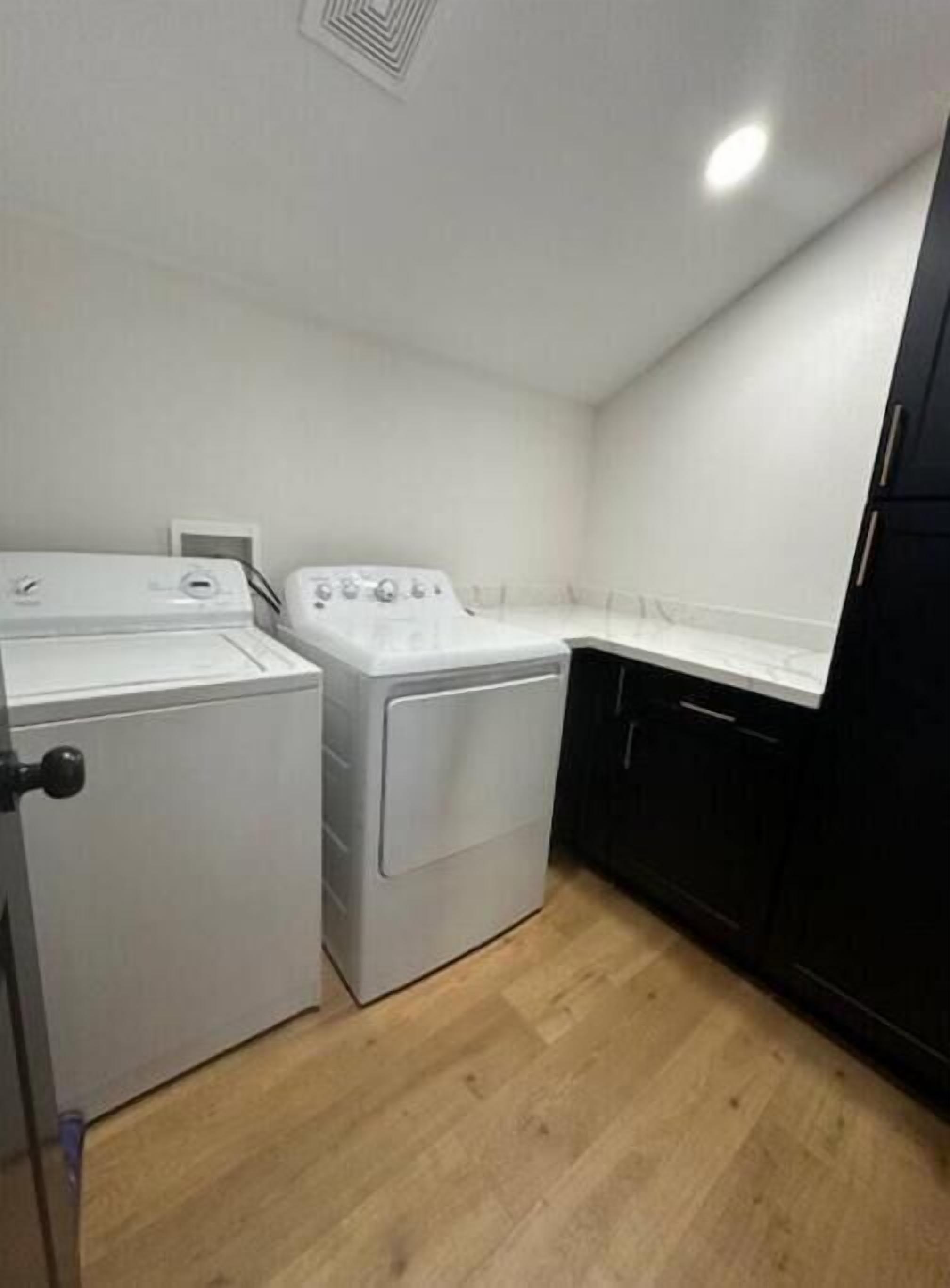Une buanderie équipée de deux machines à laver, d’un sèche-linge et de meubles de rangement noirs.