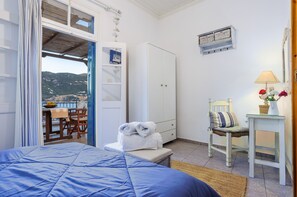 Un dormitorio con cama, armario, silla, mesa con lámpara y vistas al exterior.