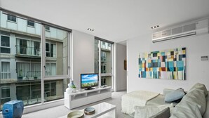 Una sala de estar moderna con un ventanal grande, un televisor de pantalla plana, un sofá blanco y un cuadro abstracto colorido en la pared.