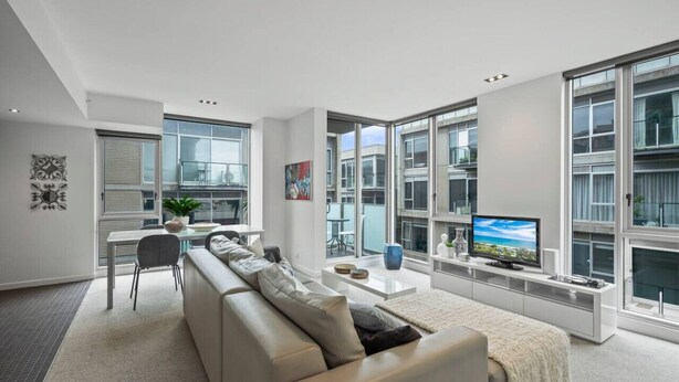 Una sala de estar moderna con sofá, televisor y ventanas amplias.
