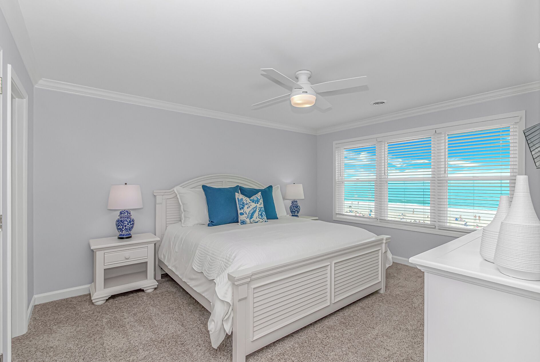 A bedroom with a bed, a ceiling fan, a window with blinds, and a nightstand with a lamp.