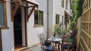 A patio with a table and chairs, surrounded by potted plants and a wooden fence. - Little Rondeval (Totnes)