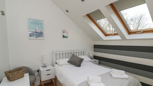 A modern bedroom with a sloped ceiling, a bed with white bedding, a bedside table with a lamp, and a view through a skylight. - Little Rondeval (Totnes)