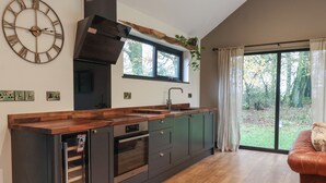 Una cocina moderna con armarios oscuros, encimera de madera y horno empotrado. Una ventana grande ofrece vistas al exterior.