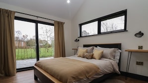 Un dormitorio con una cama grande, vistas al exterior, una ventana con persianas y una mesita de noche con una lámpara.