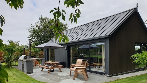 Una casa moderna con un patio, mobiliario exterior y zona de barbacoa.