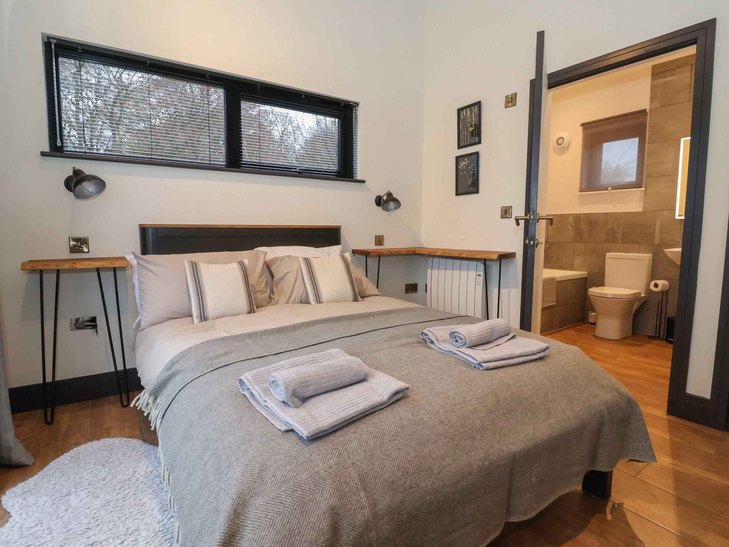 A bedroom with a bed, bedside tables, a window, and a bathroom visible through an open door.
