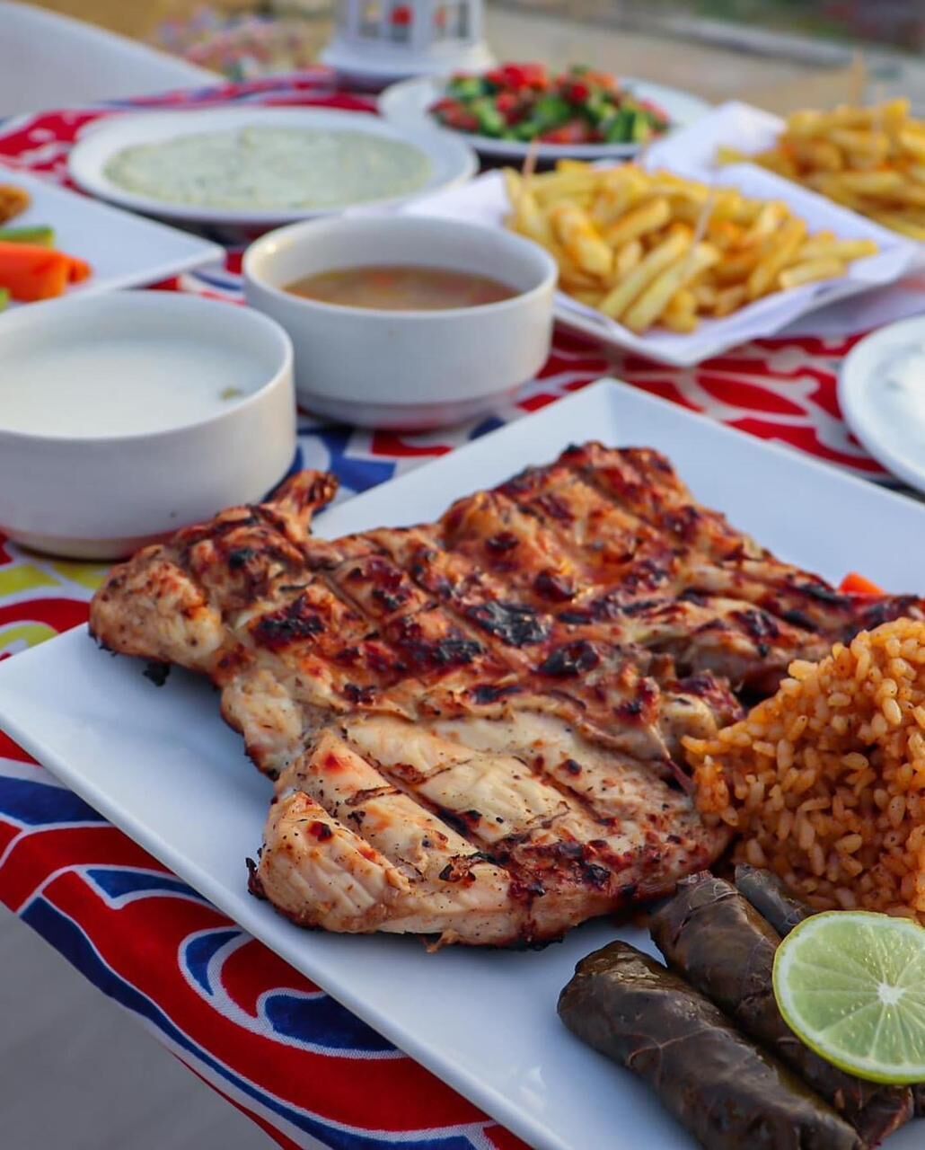 A plate of grilled chicken, rice, and stuffed grape leaves with a side of fries and salad.
