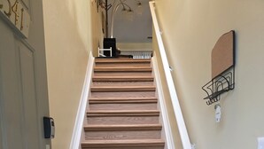 Una escalera de madera con barandillas blancas, una puerta con timbre y un aplique de pared.