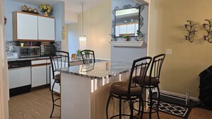 Una cocina moderna con armarios blancos, encimera de granito y una isla central con taburetes de bar.