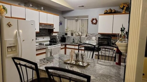 Cocina compacta con muebles blancos, encimera de mármol y comedor con cuatro sillas.