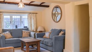 A living room with two sofas, a coffee table, a lamp, and a window with curtains. - 4 bedroom accommodation in Lymington (Lymington)