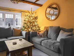 Uma sala de estar com um pinheiro de Natal, dois sofás, uma mesa de centro e um espelho redondo na parede.