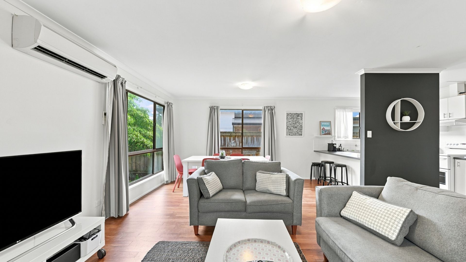 A modern living room with a flat-screen TV, two grey sofas, a coffee table, and a dining area with a table and chairs.