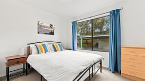 Una camera da letto con un letto, un comodino, una cassettiera, una finestra con tende e un quadro appeso al muro.