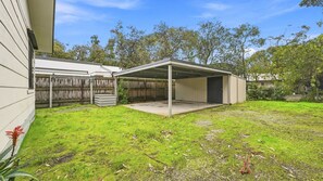 A covered outdoor area with a concrete floor, surrounded by a wooden fence and a grassy lawn.