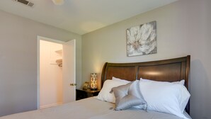 A neatly made bed with white linens and two pillows, a wooden headboard, a wall-mounted abstract art piece, and a nightstand with a lamp and a phone. - Beaumont Rental Home ~ 2 Mi to Gulf Terrace Park! (Beaumont)