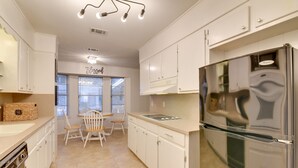 A modern kitchen with white cabinetry, a stainless steel refrigerator, and a dining area with a white table and chairs. - Beaumont Rental Home ~ 2 Mi to Gulf Terrace Park! (Beaumont)