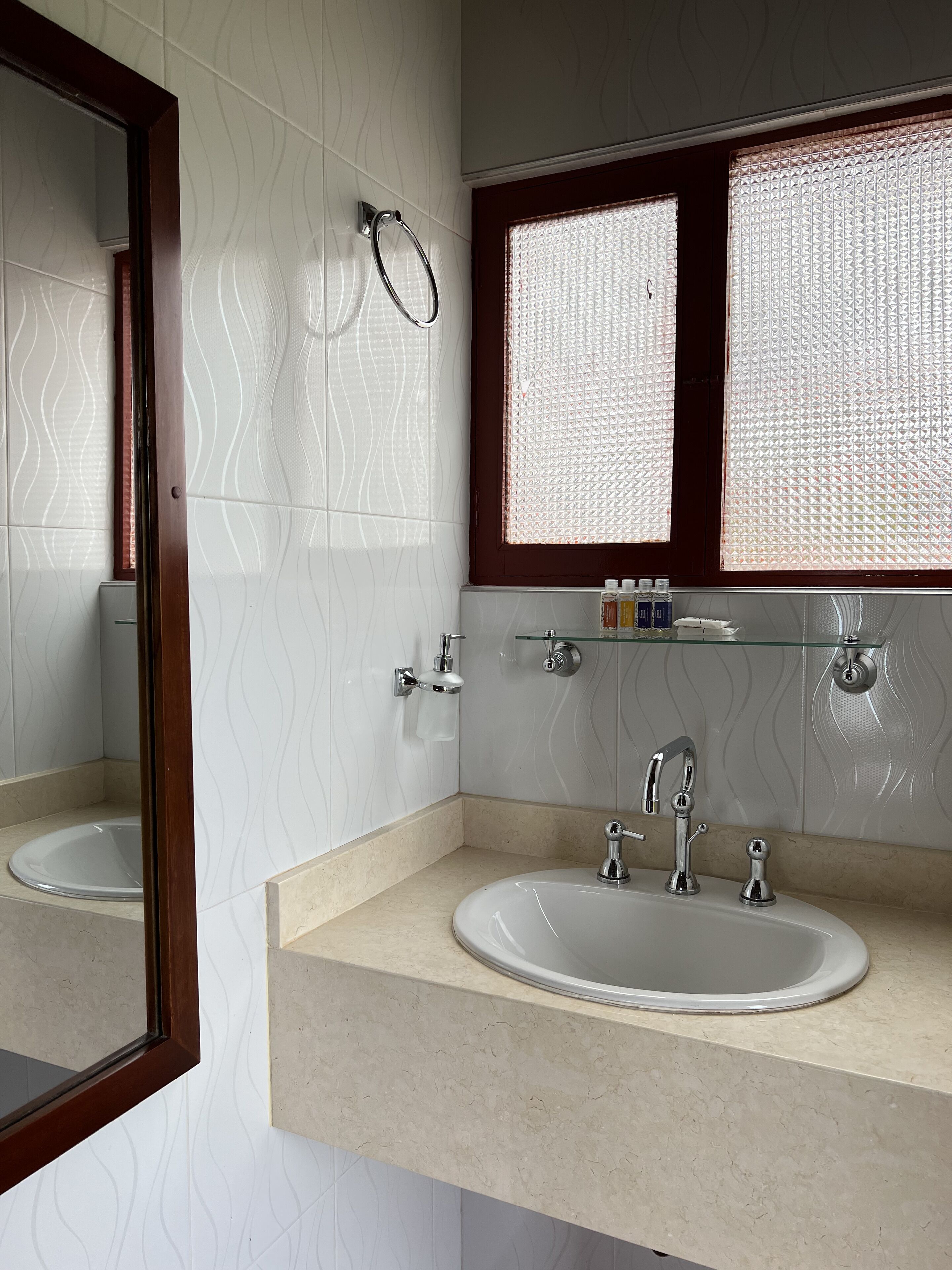A bathroom with a double sink, a mirror, a towel rack, and a window with a textured blind.