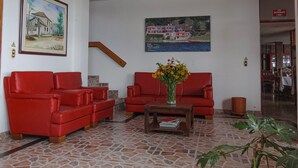 A lobby with red leather sofas, a coffee table with a vase of flowers, and two paintings on the walls.