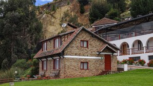 A stone house with a red door, a balcony, and a view of a mountainous landscape.