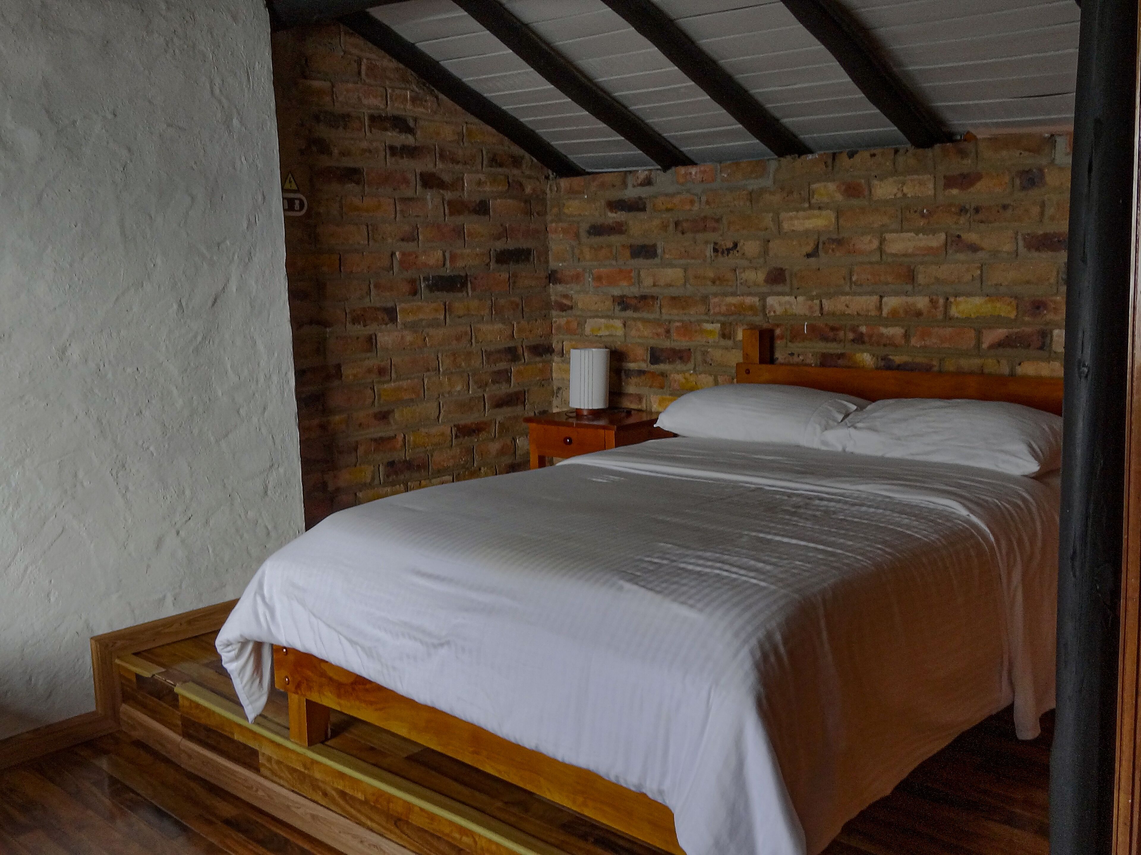 Una cama individual en una habitación con pared de ladrillo y vigas de madera.