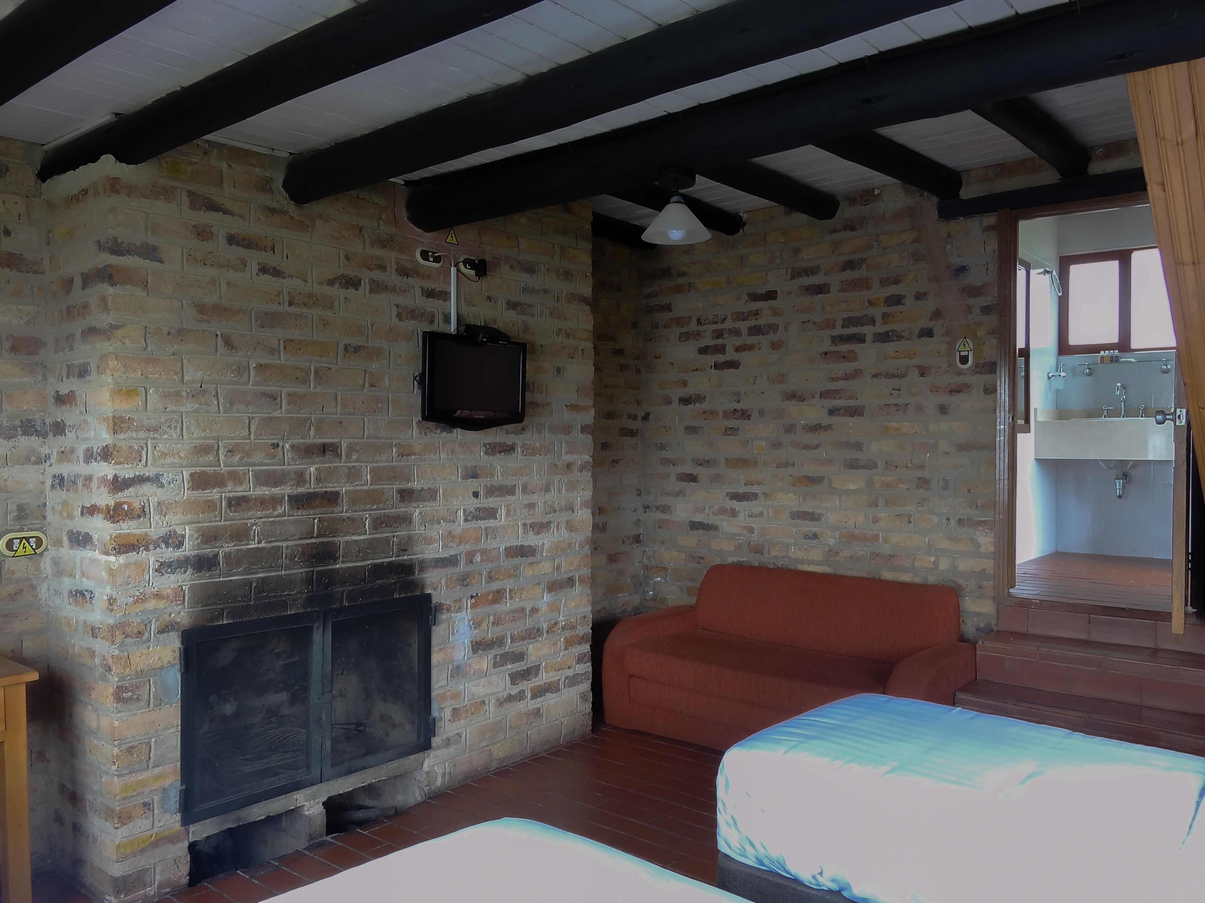Una habitación con paredes de ladrillo visto, chimenea, sofá y un televisor pequeño.