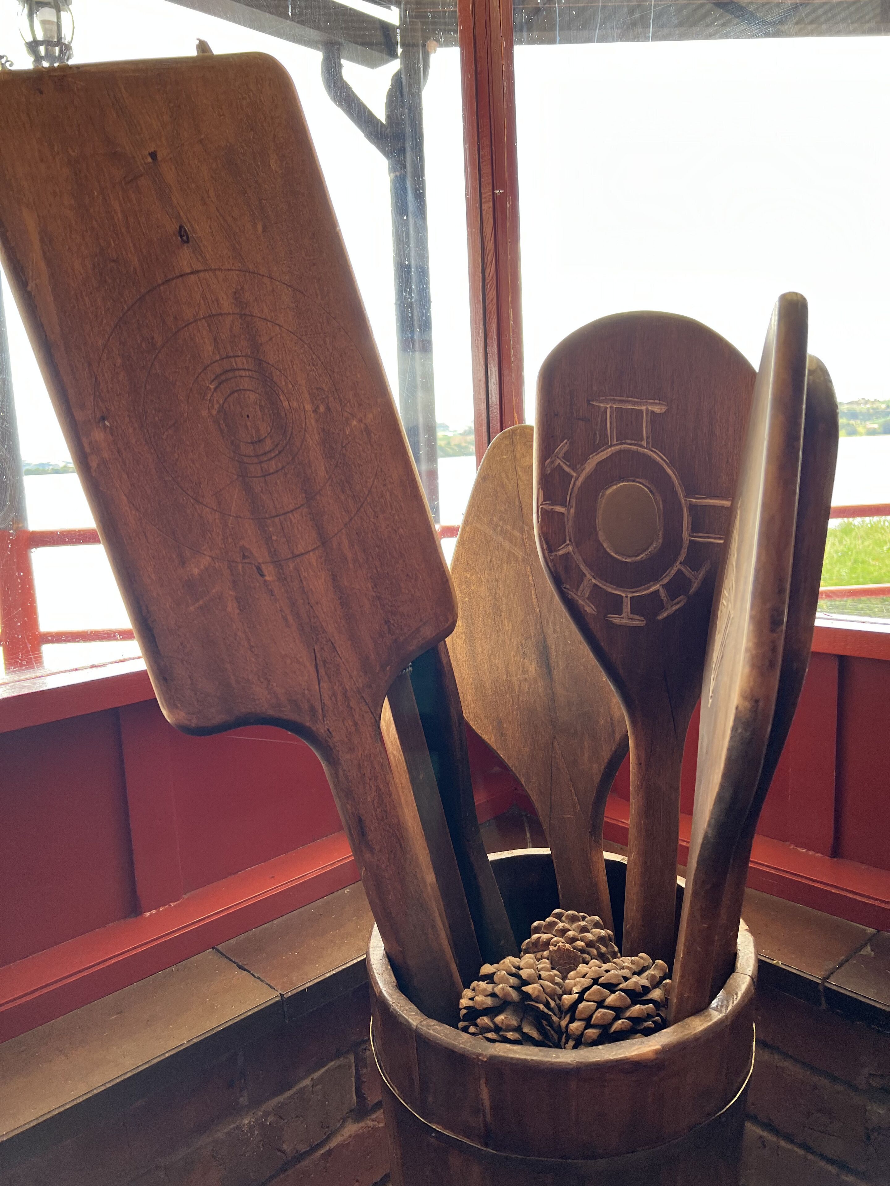 A wooden spoon holder with pinecones, located near a window with a view of a body of water.