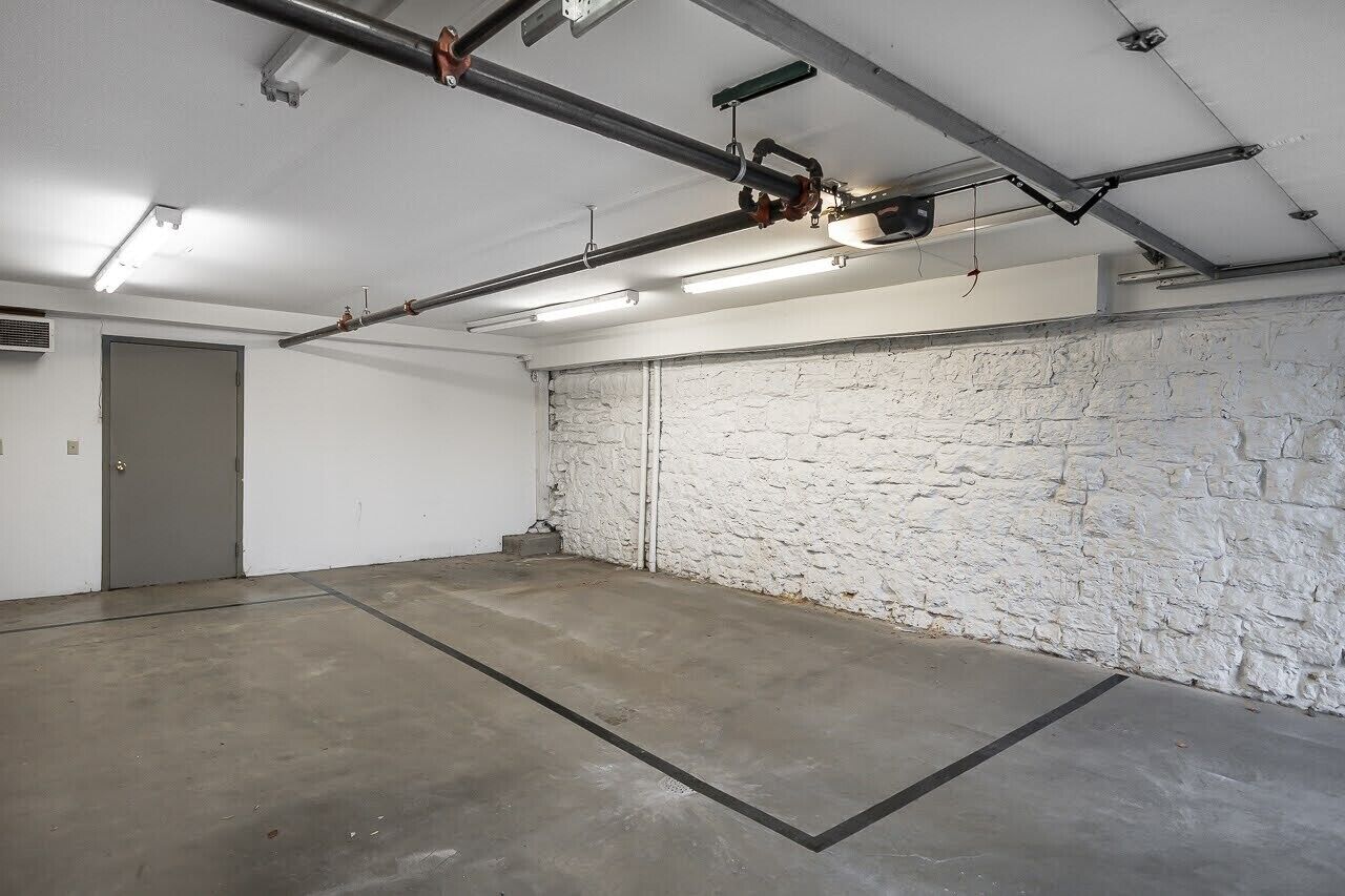 A spacious, industrial-style room with exposed pipes and a concrete floor, featuring a white brick wall and a door.