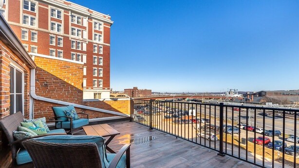 A balcony with wicker furniture and a view of a parking lot and buildings.