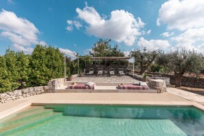A swimming pool with a sun terrace, stone walls, and outdoor seating.