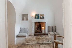 A cozy room with a fireplace, two chairs, and a small shelf with decorative items.