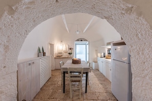 A kitchen with an arched ceiling, stone flooring, and a central dining table with chairs.