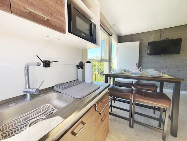A modern kitchen with a built-in oven, a sink with a soap dispenser, and a window overlooking greenery. - Caribe Studiow/wifi&AA
(Antiguo Cuscatlan)