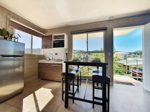 Uma cozinha moderna com geladeira de aço inoxidável, armários de madeira e uma grande janela com vista para a paisagem urbana.