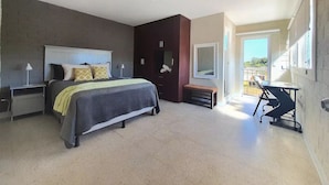 Un dormitorio moderno con cama, mesitas de noche, un banco, un escritorio y un ventanal grande.