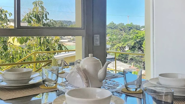Mesa de comedor dispuesta con vajilla blanca y tetera, con vista a un paisaje escénico con vegetación y un horizonte distante.