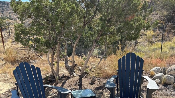 A fire pit with two Adirondack chairs and a small table in a dry, rocky outdoor setting.