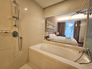 Relax in a spacious bathroom with a large bathtub and separate shower area, featuring a large mirror and a comfortable bed nearby.