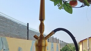 Et vandpibe med et grønt topstykke og et klart glasunderstel, placeret på en flisebelagt overflade i nærheden af en swimmingpool.