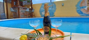 Escena junto a la piscina con una botella de Prosecco DOCG, dos copas, una bandeja y un arreglo floral.