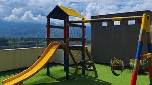 A playground with a slide and swings on a rooftop with a view of mountains.