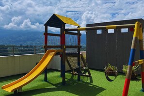 A playground with a slide and swings on a rooftop with a view of mountains.