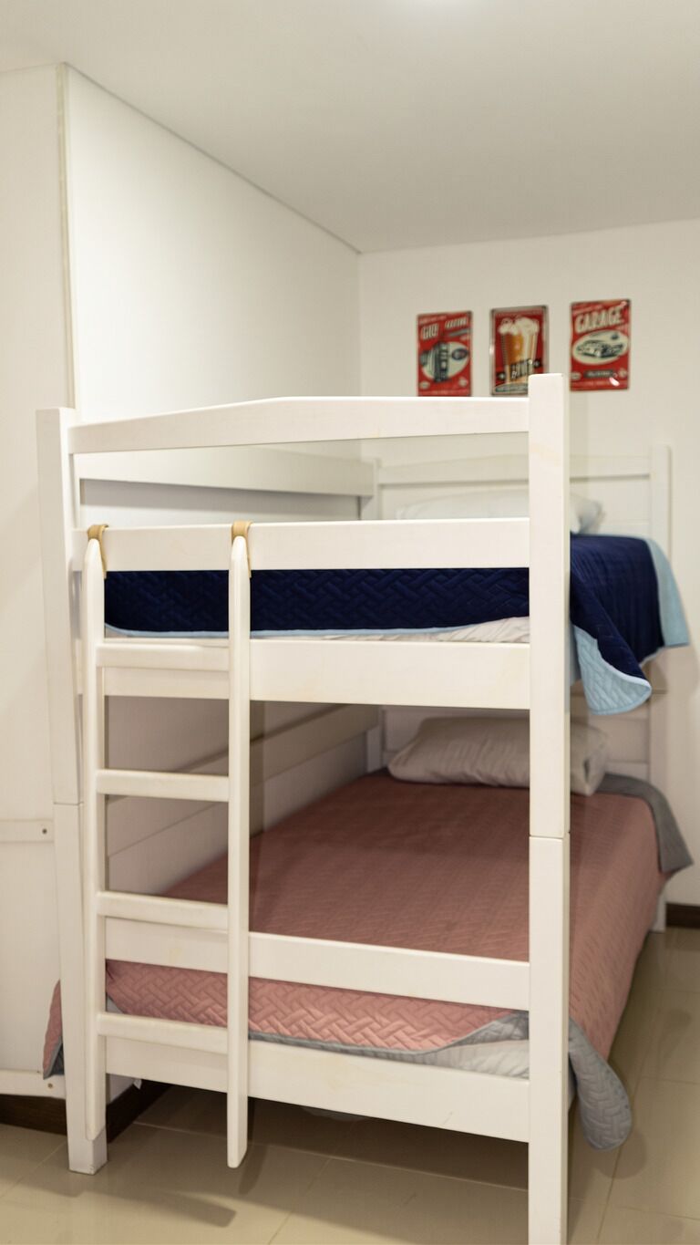 A bunk bed with a ladder, a single bed with a blue blanket, and a wall with three posters.